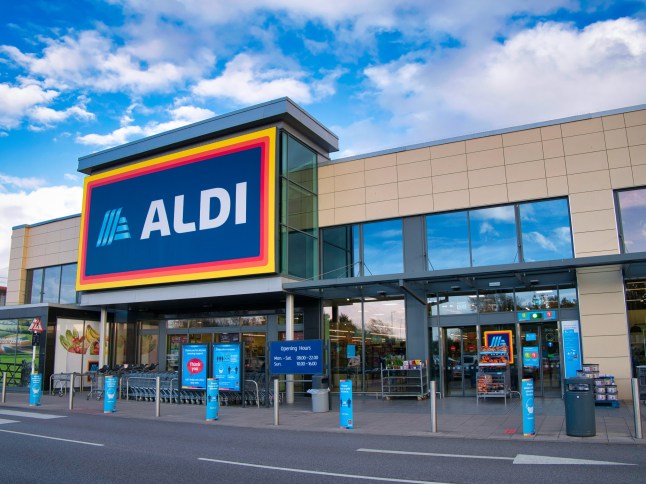 الواجهة وشعار العلامة التجارية لفرع شركة التجزئة الألمانية Aldi، تم التقاطهما في حديقة البيع بالتجزئة المحلية في ويرال، المملكة المتحدة في فترة ما بعد الظهيرة المشمسة